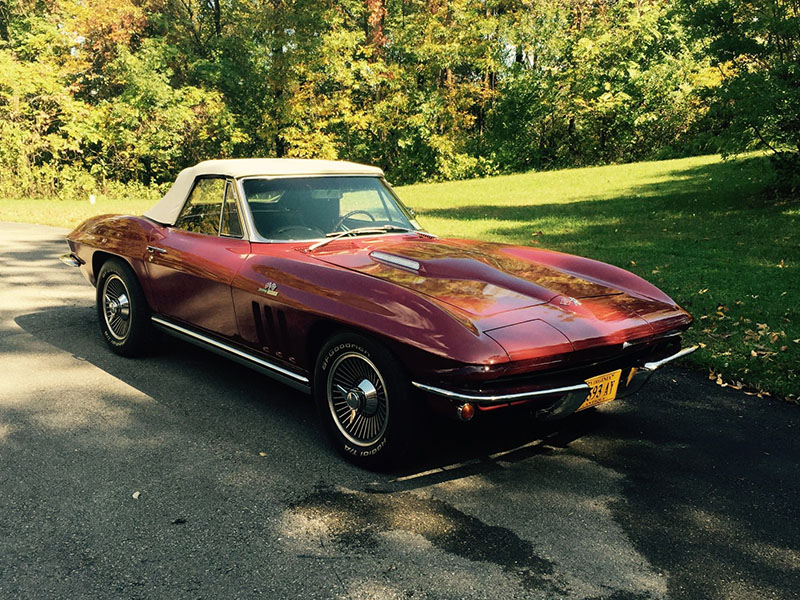 A classic red convertible collector car with a white soft top is parked on a paved driveway, surrounded by green grass and trees—perfect for any enthusiast or as a highlight at the Fall Carlisle Collector Car Auction.