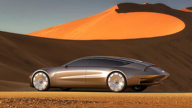 A sleek, futuristic silver Buick Electra Orbit Concept car is parked on a desert road, where '50s Jet Age meets modern minimalism against large orange sand dunes under a clear sky.