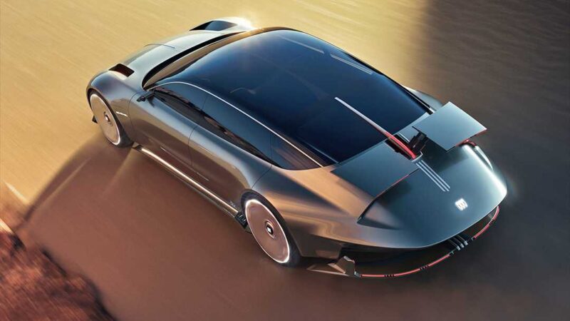 A sleek, futuristic Buick Electra Orbit Concept—with a large rear wing and dark tinted windows—drives on a road, viewed from above, where '50s Jet Age meets modern minimalism.