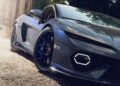 Close-up view of the front side of a dark gray Lamborghini Bespoke Temerario sports car parked on a gravel surface in Porto Cervo, showcasing its headlight, wheel, and sleek body design.