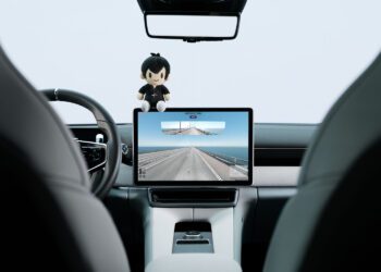 Interior view of a car’s dashboard and steering wheel, with a touchscreen displaying a road—perfect for a GeoGuessr game competition. A doll sits on top of the screen in this unique Polestar Edition cabin.