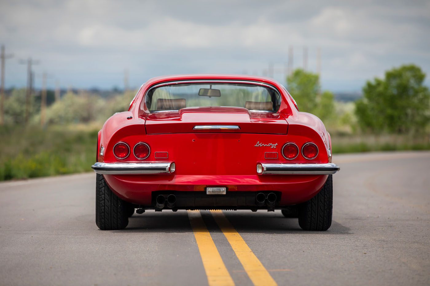 Rear view of a classic red sports car, reminiscent of Ferrari Legends, parked on a paved road in Monterey, with trees and a cloudy sky in the background—an iconic scene ready for Mecum Auction.