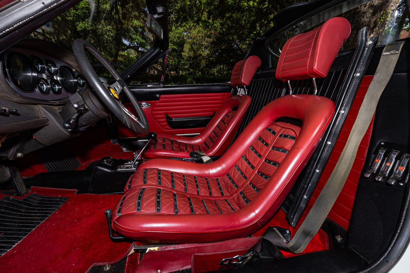 Vintage car interior featuring red leather bucket seats with black accents, classic dashboard, and manual gear shift, photographed in natural daylight—an iconic example destined for Mecum’s 2025 Auction in Monterey.
