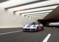 A white Porsche 935 with red and blue stripes, a true dream car, speeds through a modern tunnel on an empty highway.