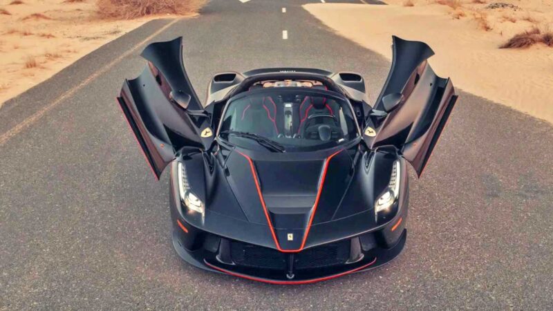 A black Ferrari sports car with its butterfly doors open is parked on a desert road, viewed from above—a fitting contender for the 10 Most Expensive Cars To Sell At 2025 Monterey Car Week Auctions.