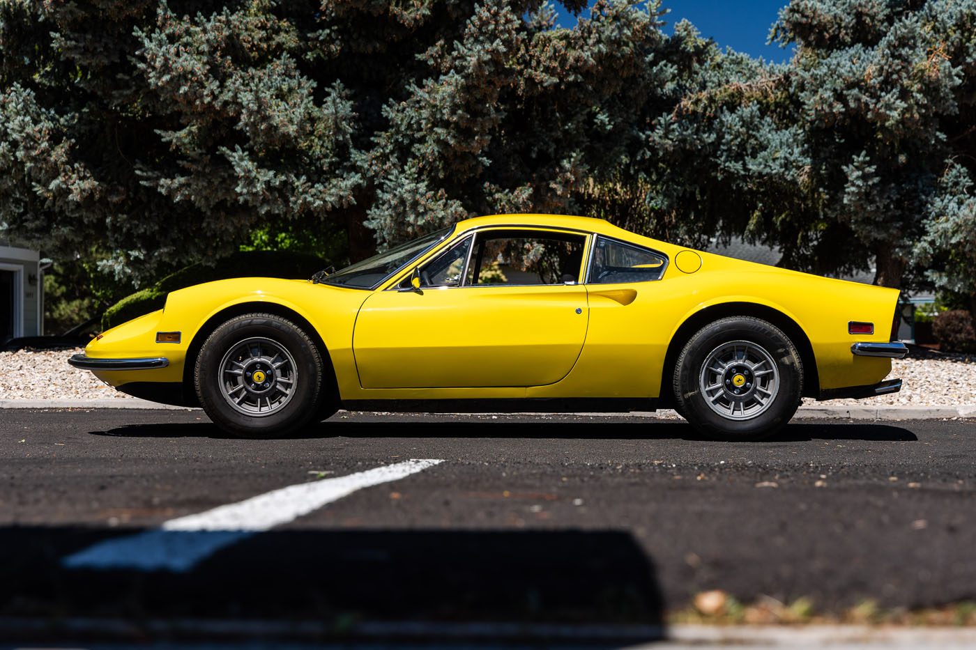 A yellow classic sports car, a nod to Ferrari Legends, is parked on a paved road with trees in the background, viewed from the side—capturing the allure of Monterey before Mecum’s 2025 Auction.