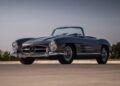 A classic black Mercedes-Benz convertible sports car, a true million-dollar car, parked on a paved surface with trees and sky in the background—an icon ready for the Mecum Monterey 2025 Auction.