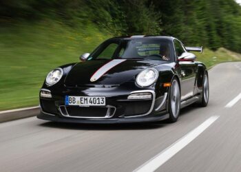 A black 997 Porsche 911 GT3 RS 4.0 with red and white stripes drives on a winding road bordered by greenery and trees.