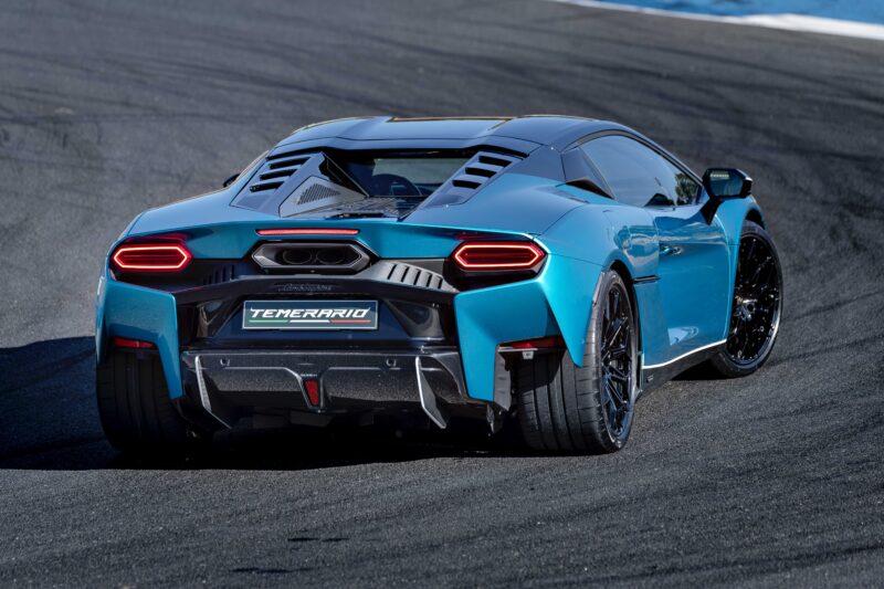 A blue sports car with black accents is seen from the rear on a racetrack. Aerodynamic vents, dual exhausts, and "TEMERARIO" on the license plate area hint at a Track Review: Lamborghini Temerario might just outshine V12 Revuelto.