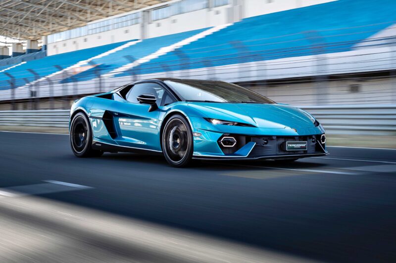 A blue sports car drives on a racetrack with blurred motion in the background and empty grandstand seats, evoking a Track Review: Lamborghini Temerario might just outshine V12 Revuelto.