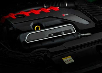 Close-up view of a modern car engine with a red engine cover, black components, and visible warning label—The Last Surviving 5-Cylinder On Sale Today Packs A Punch under the hood.