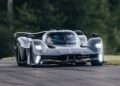 A sleek, black Aston Martin Valkyrie from Miller Motorcars tears down Monticello Raceway, its high-performance design contrasting beautifully with the lush greenery in the background.