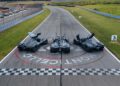 Three black sports cars with open doors, including an Aston Martin Valkyrie, are parked on the starting line at Monticello Motor Club. This thrilling scene captures the excitement of a Miller Motorcars showcase at the famed racetrack.