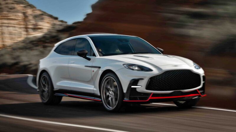 A white luxury SUV with black and red accents drives on a winding mountain road, capturing the adventurous spirit of Aston Martin Marks 75 Years in the Americas with Thrillseeker Collection and Valhalla Debut at Monterey.