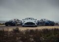 Three convertible sports cars are parked side by side on a dirt road near the ocean under a cloudy sky, reminiscent of Aston Martin marking 75 years in the Americas with its Thrillseeker Collection and Valhalla debut at Monterey.
