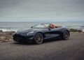 A black convertible sports car with orange interior is parked on a coastal road, echoing the thrill of Aston Martin marking 75 years in the Americas with the Thrillseeker Collection and Valhalla debut at Monterey.