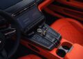 Close-up view of a luxury car's center console with a touchscreen display, various control buttons, and orange leather upholstery—showcasing the refined craftsmanship seen in the Aston Martin Marks 75 Years in the Americas collection.