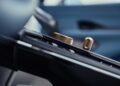 Close-up view of a car's center console featuring metallic dials and buttons, with a blurred car door in the background—capturing the luxury spirit as Aston Martin marks 75 years in the Americas with its Thrillseeker Collection.