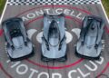 Three grey high-performance sports cars, including an Aston Martin Valkyrie, are parked side by side on the racetrack at Monticello Motor Club, viewed from above—an impressive lineup possibly showcased by Miller Motorcars.