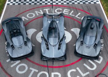 Three grey high-performance sports cars, including an Aston Martin Valkyrie, are parked side by side on the racetrack at Monticello Motor Club, viewed from above—an impressive lineup possibly showcased by Miller Motorcars.
