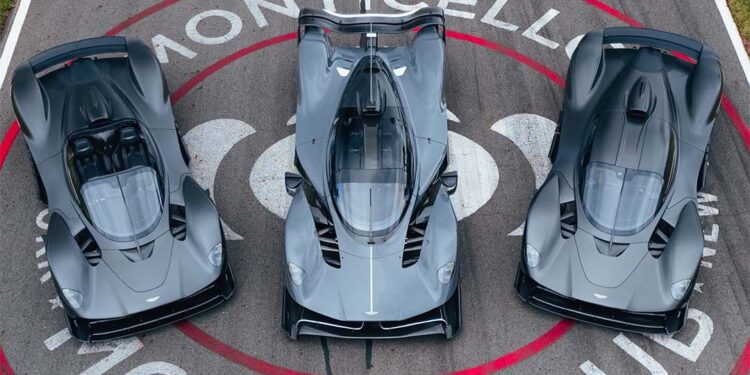 Three grey high-performance sports cars, including an Aston Martin Valkyrie, are parked side by side on the racetrack at Monticello Motor Club, viewed from above—an impressive lineup possibly showcased by Miller Motorcars.
