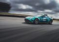 A teal Aston Martin sports car with "F1" and "aramco" logos drives on a racetrack under a cloudy sky.