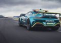A green Aston Martin Vantage Safety Car with "aramco" branding drives on a racetrack under a cloudy sky, equipped with an orange roof light bar during a Formula 1 event.