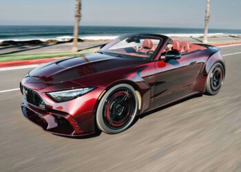 The BRABUS Rocket GTC Deep Red breaks cover at Pebble Beach, as a red convertible sports car with a black grille and red interior drives along a coastal road, ocean and palm trees in the backdrop—boasting 1000 HP and an all-carbon body.