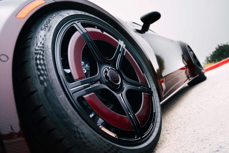 Close-up view of a custom black and red sports car wheel with Brabus branding, inspired by the BRABUS Rocket GTC Deep Red that breaks cover at Pebble Beach with 1000 HP and an all-carbon body, parked on a paved surface with blurred background.