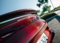 Close-up of the rear end of a red car with a carbon fiber spoiler, "Genesis" badge, and a California license plate, echoing the bold style of the BRABUS Rocket GTC Deep Red that broke cover at Pebble Beach with its 1000 HP all-carbon body.
