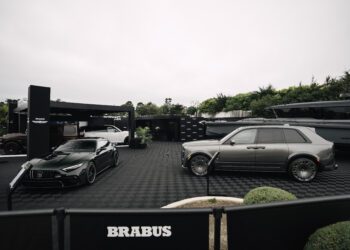 Two luxury cars—a dark green sports car and a silver SUV—are showcased in the outdoor BRABUS exhibition area at Pebble Beach, with a yacht and lush greenery completing the stylish backdrop.