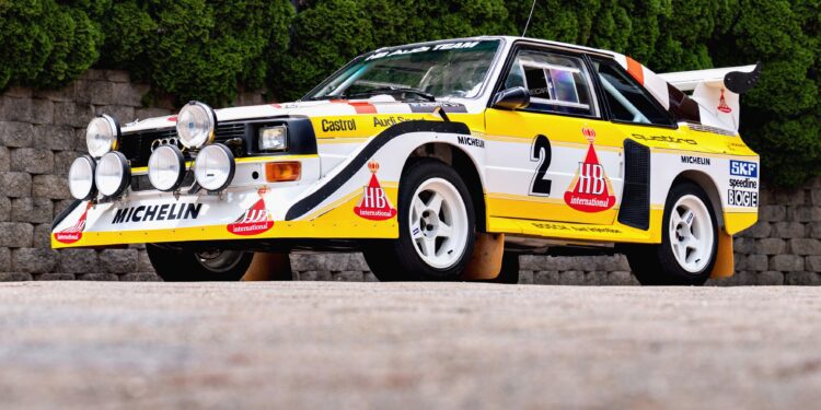 A white and yellow rally car with sponsor logos and multiple front-mounted spotlights is parked on a paved surface, highlighted as one of the 2025 Bonhams Monterey: 10 Must-See Cars Crossing the Block at The Quail.