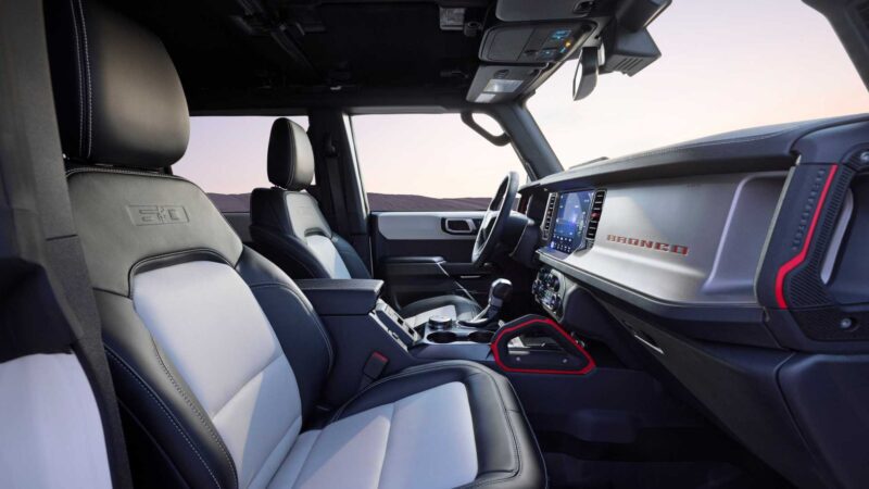 Interior view of a modern off-road vehicle—possibly the Bronco Turns 60: Ford Reveals Heritage Edition for 2026—with black and gray leather seats, a digital dashboard, and gear levers, framed by a desert landscape through the windows.