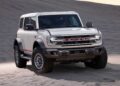A white Ford Bronco SUV, celebrating Bronco Turns 60: Ford Reveals Heritage Edition for 2026, is parked on sand dunes under a clear sky.