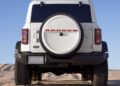 A white Ford Bronco SUV is parked on sand, viewed from the rear, with a spare tire mounted on the back and the Bronco logo visible—a nod to Bronco Turns 60: Ford Reveals Heritage Edition for 2026.