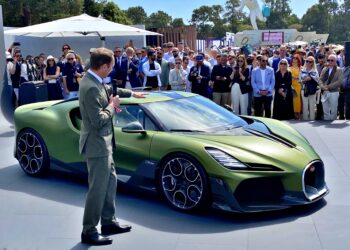 A man in a suit presents a green Bugatti sports car to a crowd at an outdoor event on a sunny day.