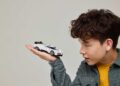 A boy holds a small white toy car in his hand and looks at it closely against a plain background, capturing the excitement as LEGO and Bugatti unite to celebrate the iconic Centodieci.