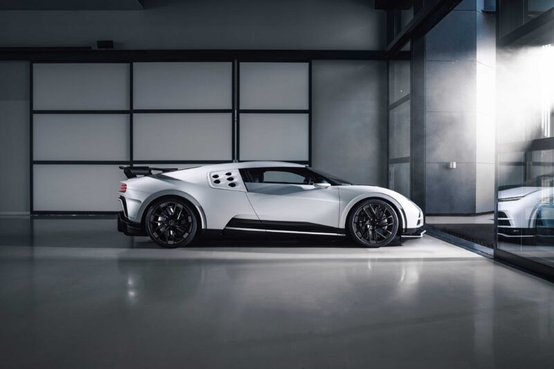 A white sports car with black wheels, inspired by the collaboration where LEGO and Bugatti unite to celebrate the iconic Centodieci, is parked in a modern, minimalistic garage with large windows and polished floors.