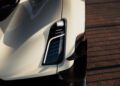 Close-up of a modern car’s front left headlight and bumper, showcasing sleek design and aerodynamic details in sunlight.