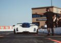 A white futuristic race car is stopped on a track while a person wearing headphones directs it at Sonoma Raceway.