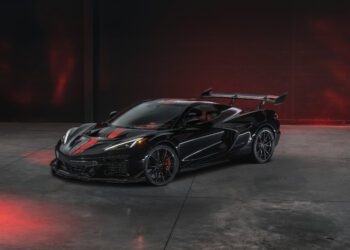 A black Chevrolet Corvette ZR1X hypercar with red accents and a large rear wing is parked in an empty, dimly lit garage with striking red lighting effects.