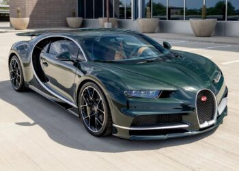 A dark green Bugatti Chiron hypercar is parked outdoors on a concrete surface near a modern building with large windows and potted plants.