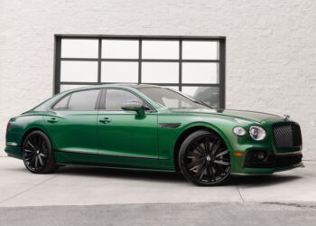 A green Bentley Continental GT End of Era Edition luxury sedan parked on a concrete driveway in front of a large window with a black frame.