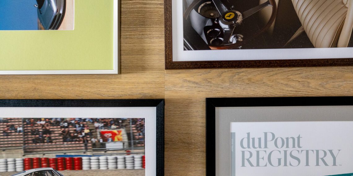 Five pieces of wall decor, including four framed automotive-themed photos and a magazine cover, are arranged in a grid pattern to add automotive flair to the wooden wall.