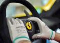 Gloved hands hold a Ferrari Daytona SP3 steering wheel, with the yellow Ferrari logo visible at the center—an experience fit for a billionaire.