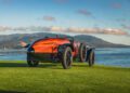 A vintage Hispano-Suiza with a polished wooden body is parked on grass near water, mountains, and a blue sky—capturing the elegance of a Pebble Beach Concours d’Elegance Best of Show moment.