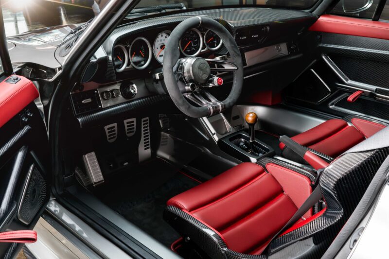 Interior of a modern sports car featuring red and black seats, a manual gear shift, and leather-wrapped steering wheel—reminiscent of the exclusivity found in Gunther Werks Unveils Limited Edition 1000-HP Slantnose-Inspired F-26 at The Quail.