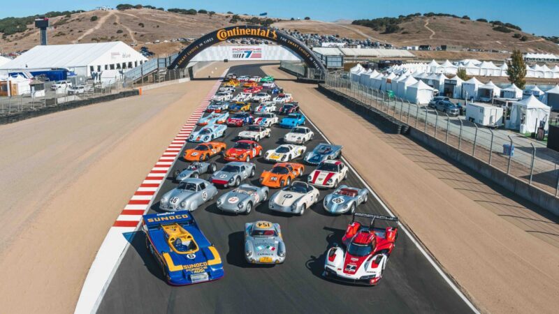 A group of vintage and modern race cars lined up on a racetrack under a Continental Tire arch at Monterey Car Week 2025, with tents and hills in the background—a scene worthy of the duPont REGISTRY.