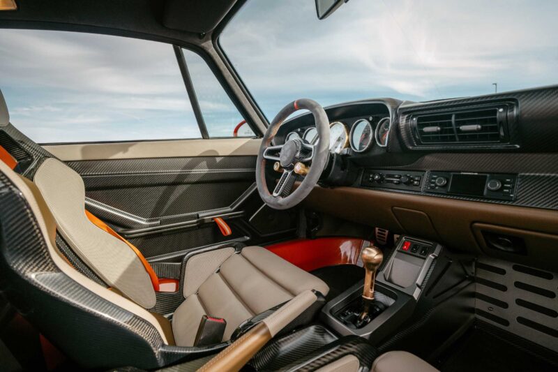 Interior of a Gunther Werks Turbo Tested: Bar None The Gnarliest Porsche Restomod Yet, featuring a modern dashboard, round gauges, sports seat, and manual gear shifter as seen from the driver's side.