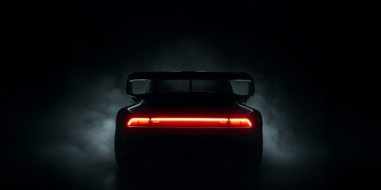 A rear view of a Slantnose-inspired sports car with a large spoiler, illuminated by its red taillight, surrounded by darkness and faint smoke—an unmistakable Gunther Werks presence at The Quail.
